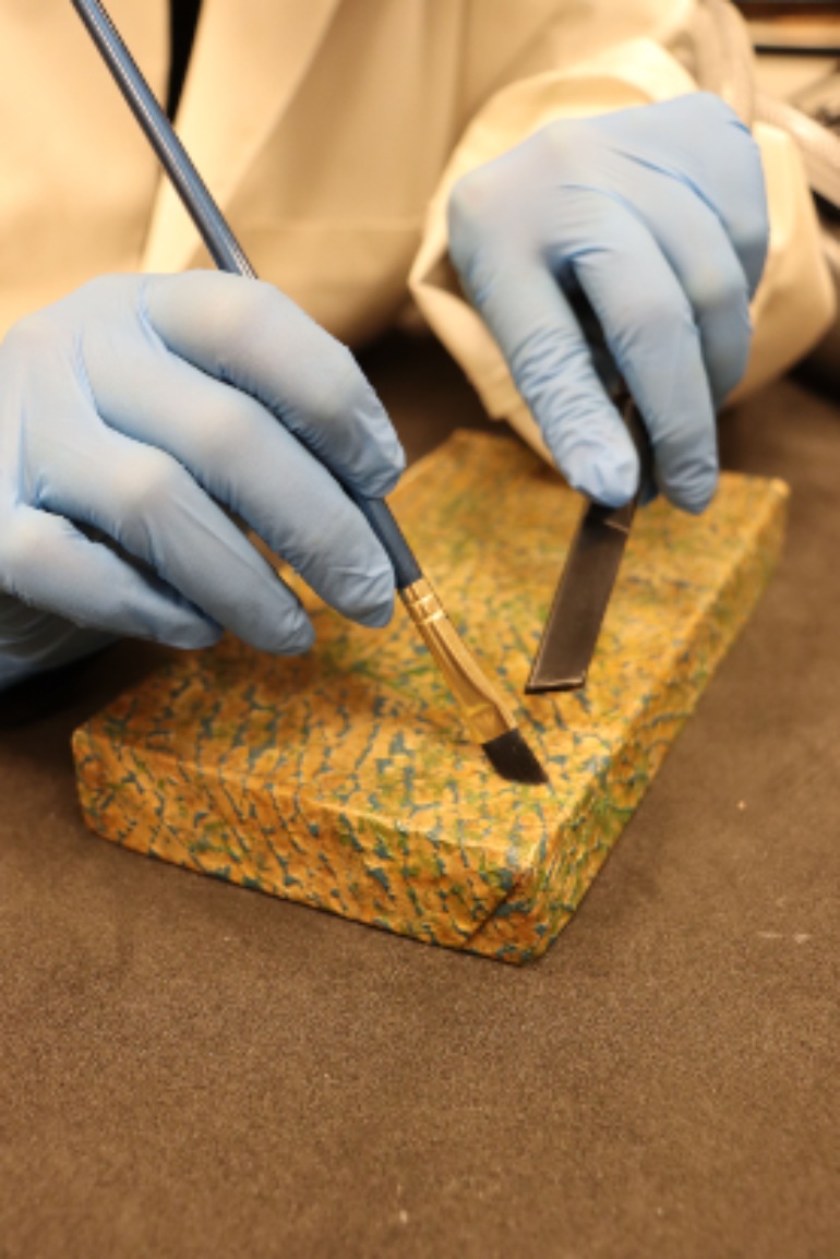 Curators wears blue gloves and cleans a card box using a fine dry brush and vacuum nozzle 