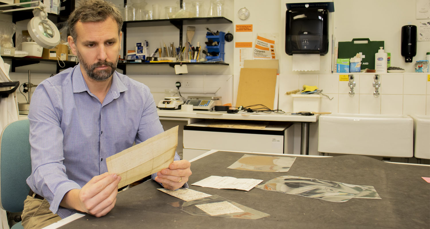 Collections Information Officer Nico Tyack looking at 18th century tavern bills in the Museum Collections Centre conservation lab.jpg