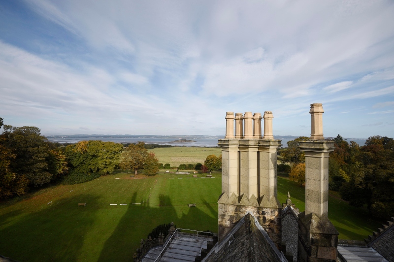 View from the roof of Lauriston Castle. Blue sky and white clouds with the River Forth in the background and chimney pots and green lawn in the foreground