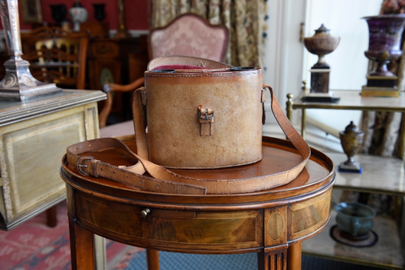 Brown leather binocular case sits on top of a small oval mahogany table