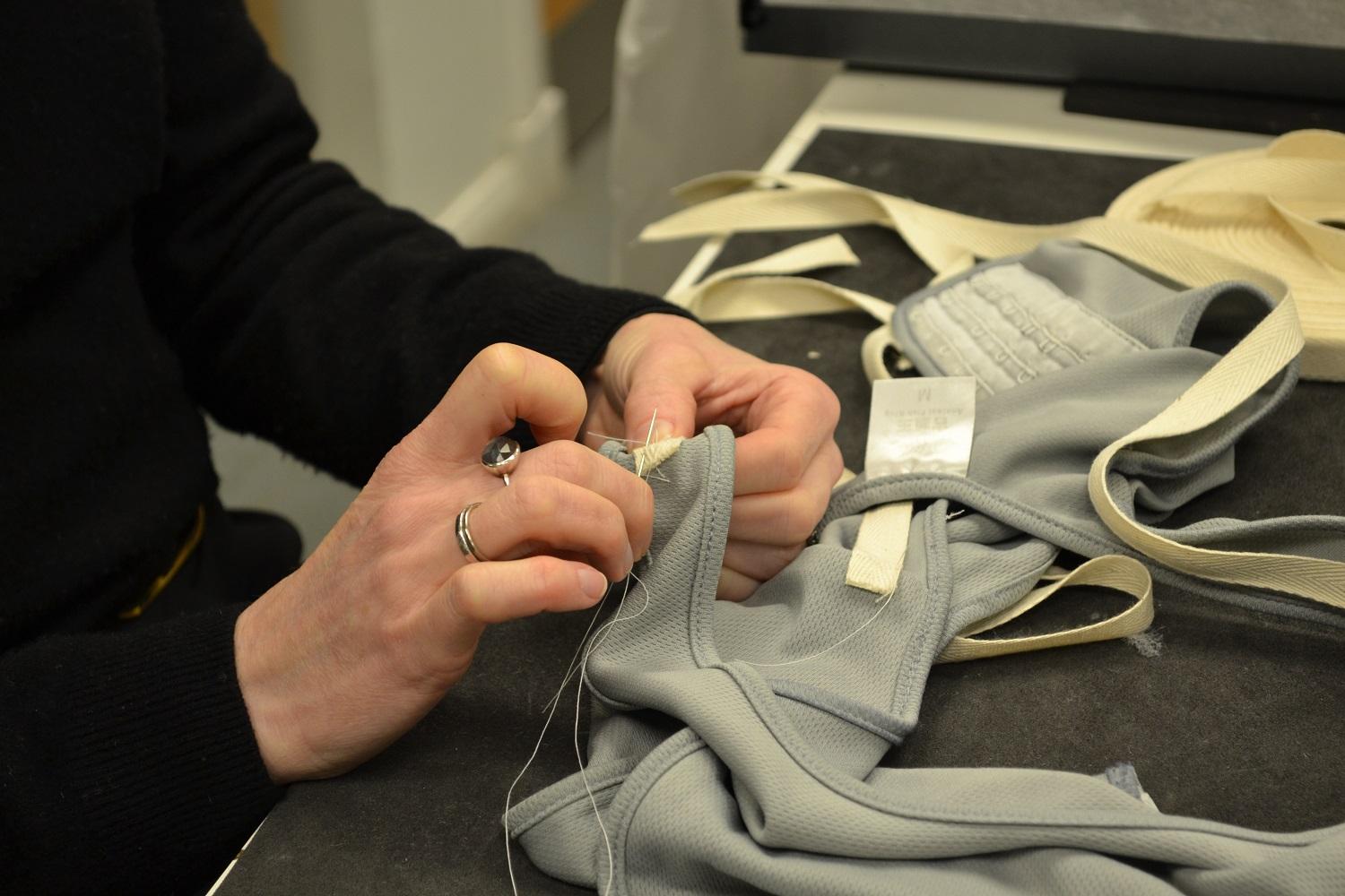 Curator stitching label onto textile object