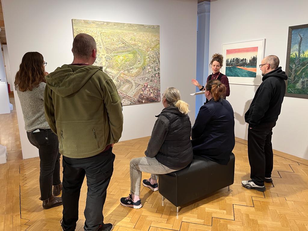 A group of people listen to the curator and admire artwork on display at the City Art Centre