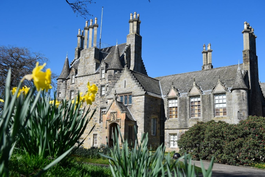 Lauriston Castle underneath a blue sky. Yellow daffodils feature in the foreground