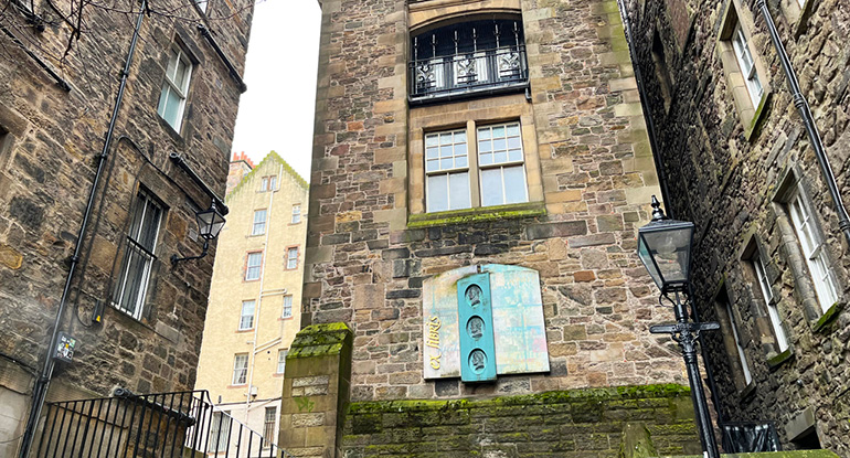 Stone buildings at the entrance to Makars' Court. Black Victorian lamp post appears in the foreground