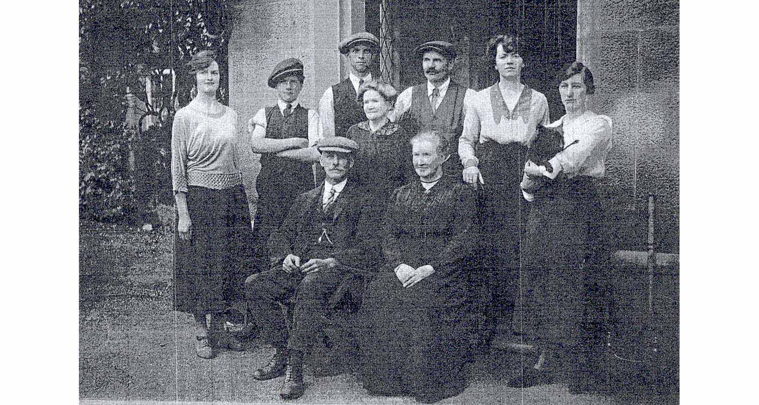 A group of people standing posing in the doorway porch of a large house