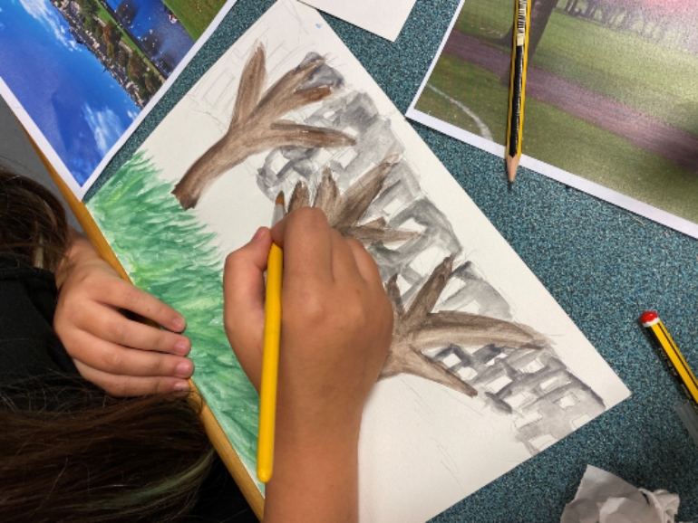 Photograph of a child painting a picture of trees and grass on a white piece of paper