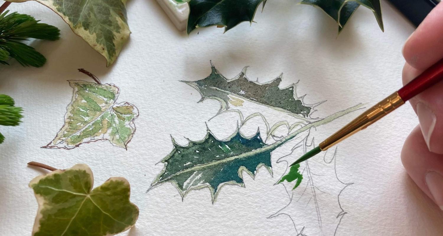 Photo of a person painting ivy and holly leaves on a  piece of white paper