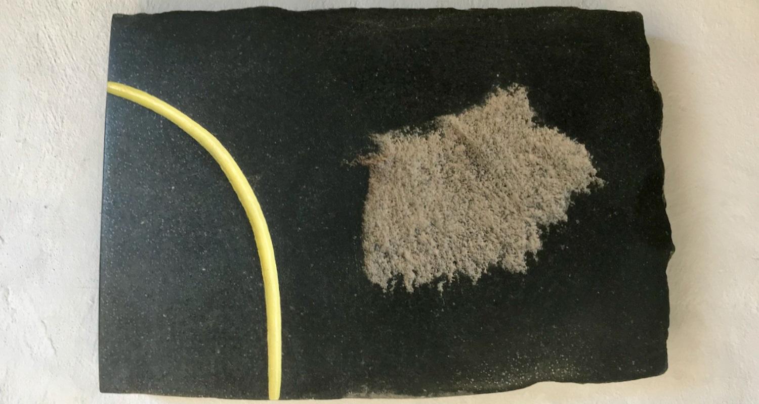 A rectangle of carved basalt, a curve of yellow enamel paint, and wax