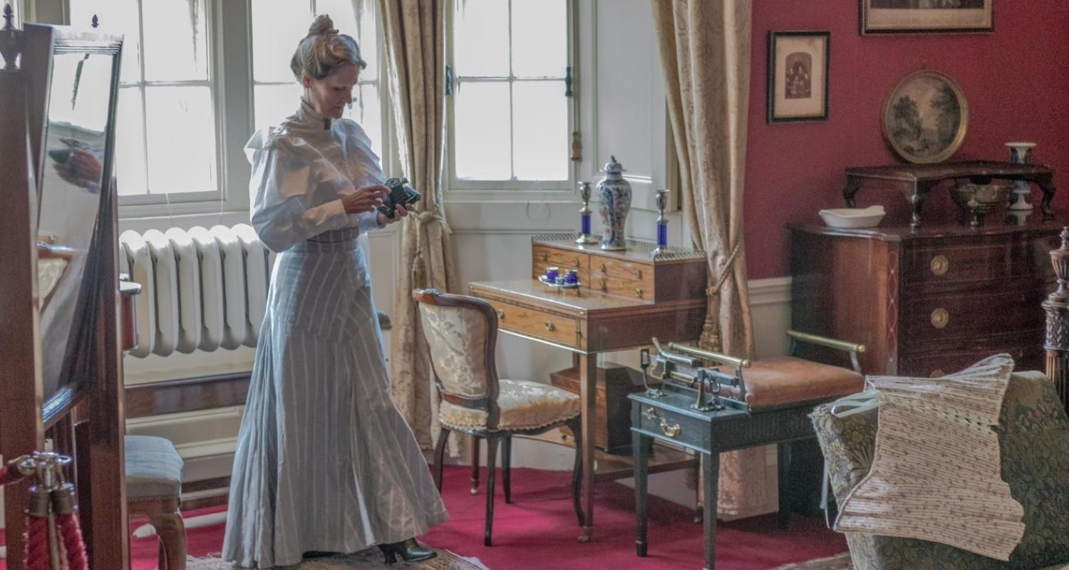 A costumed peformer holds an old camera in front of a window