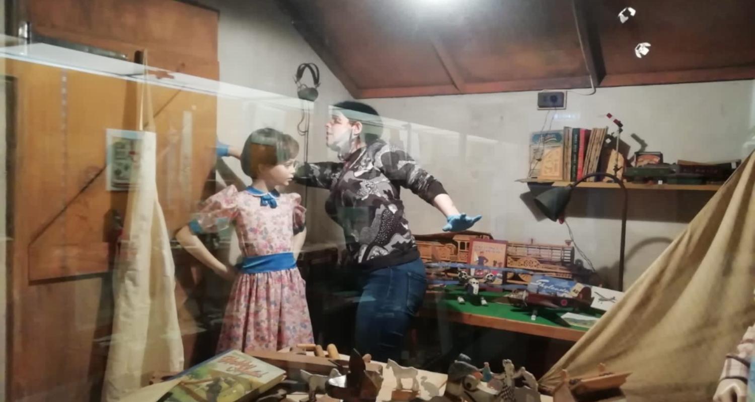 Curator working inside a display case beside a mannequin