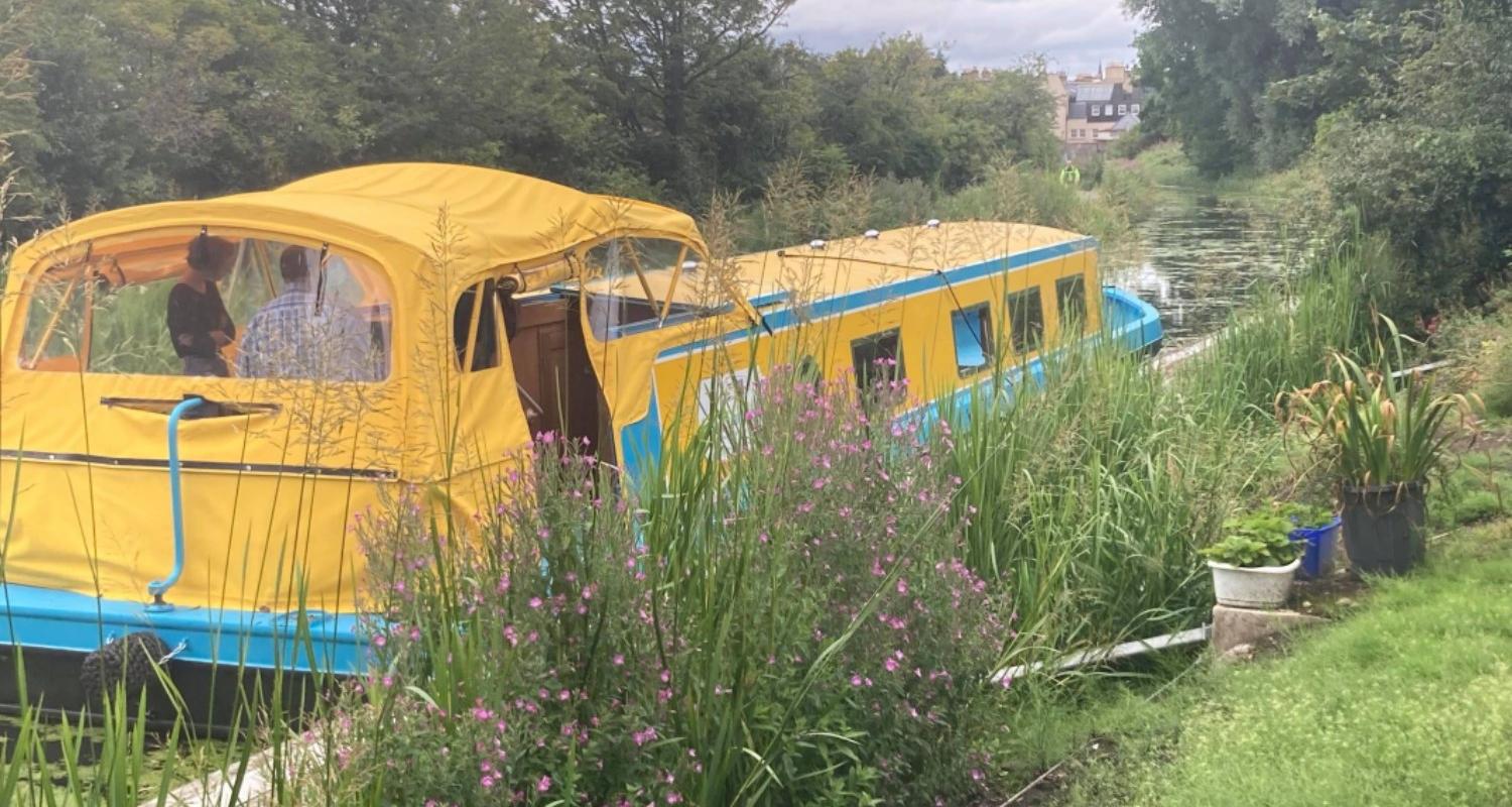 Yellow and blue long boat sitting on a canal surrounded by greenery. Part of the Museums & Galleries Edinburgh Discover Lothian project. 