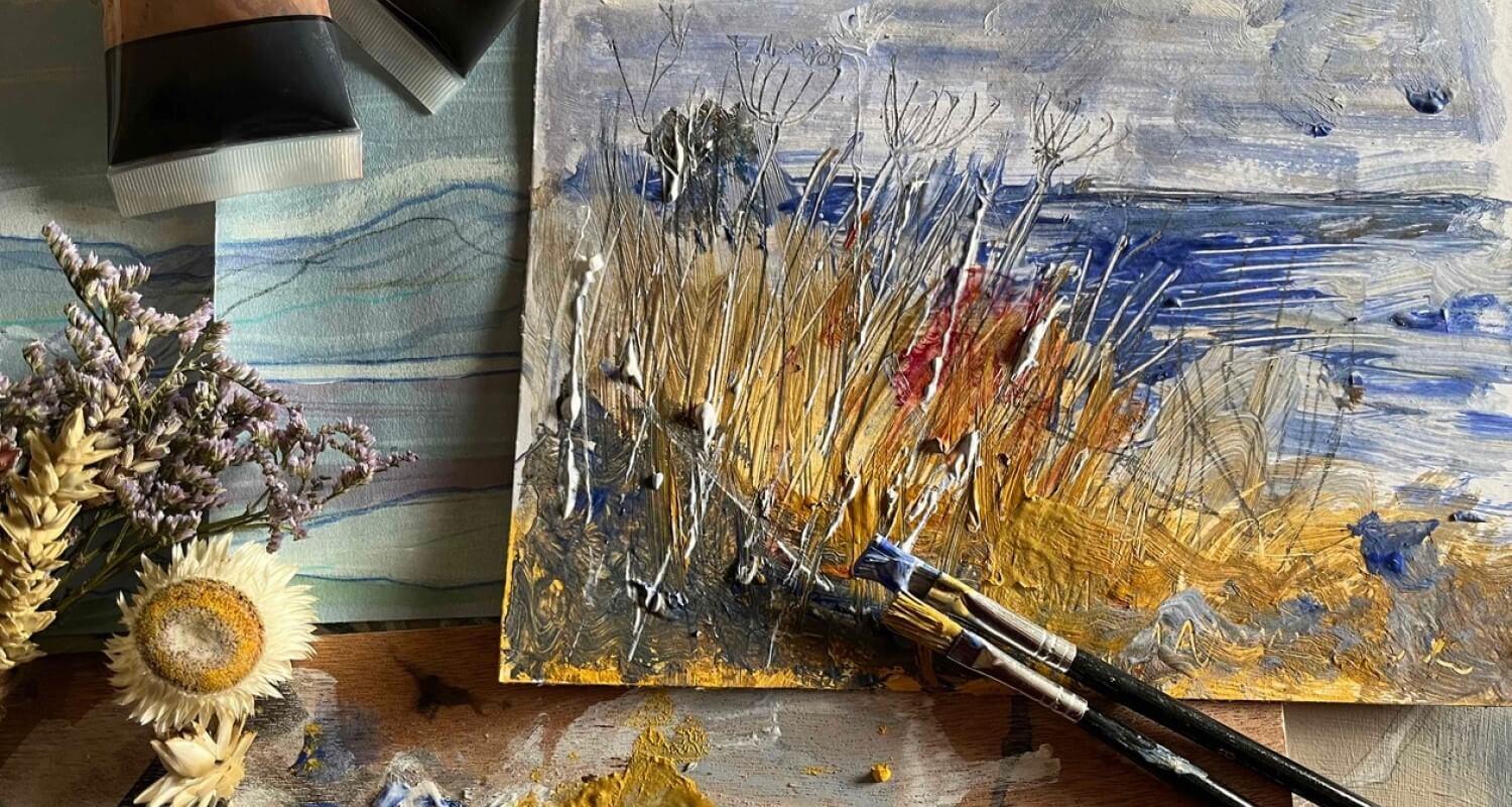 An oil painting of a stormy seascape from grassy dunes with paints and brushes lying beside it