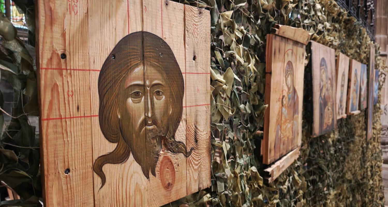 A row of ammo box lids with religious images on them attached to a camouflaged fence