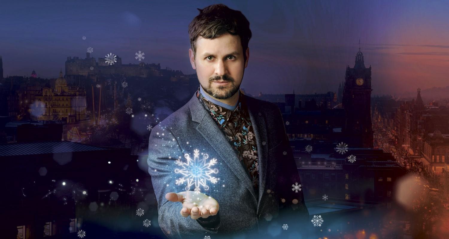 A bearded man stands in front of a dusk backdrop of Edinburgh Castle and Princes Street as a stylised giant snowflake hovers above his outstretched hand