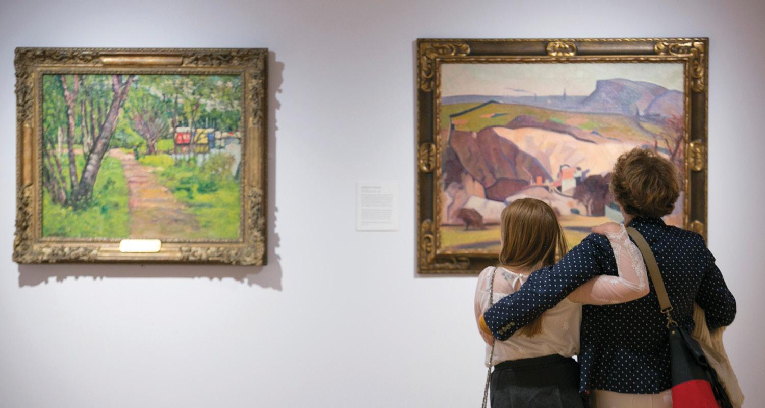 Mother and daughter stand with their arms around each other admiring two paintings on display in the gallery