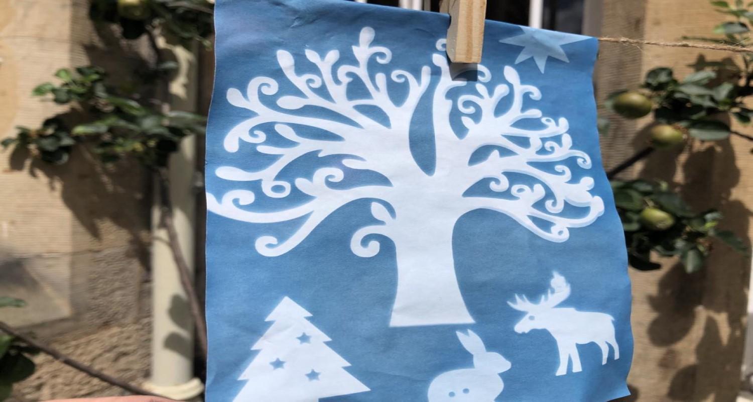 A white tree, Xmas tree, stag and rabbit on a blue sheet of paper pegged onto a washing line