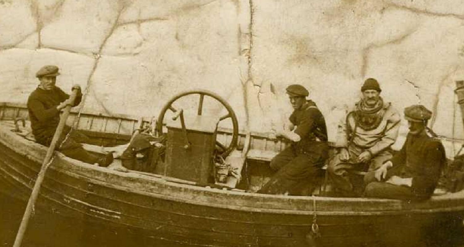 Sepia photograph of four men in a boat, one in a full diving suit.