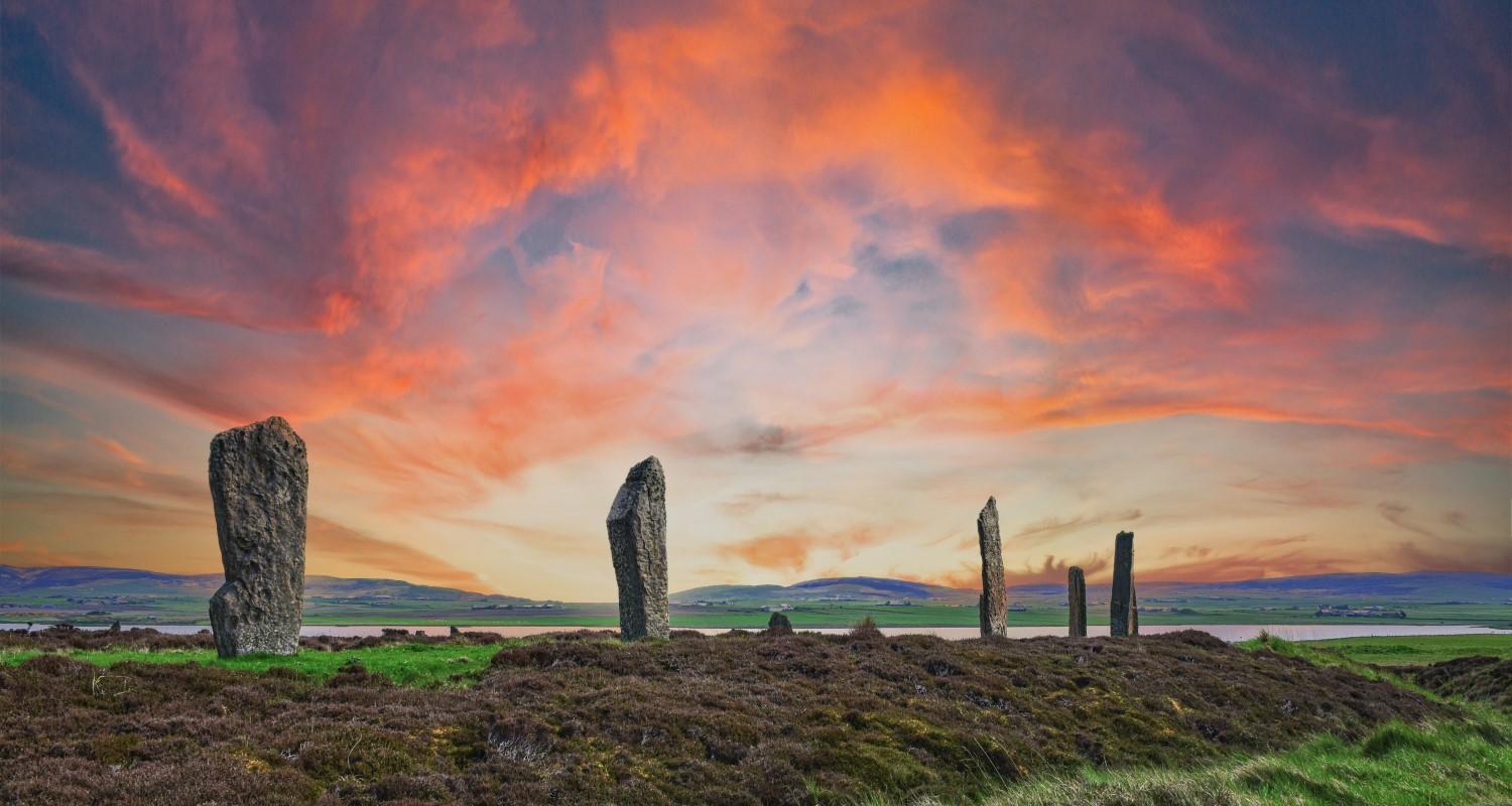 Standing stones on a grassy hillside against a red sunset