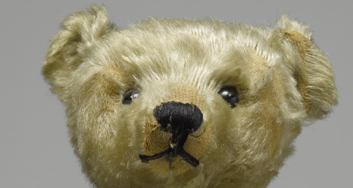Close up of the head of a light brown teddy bear