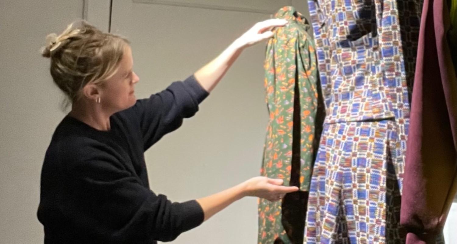 Curator Vicky Garrington stands beside a display of women's wartime dresses