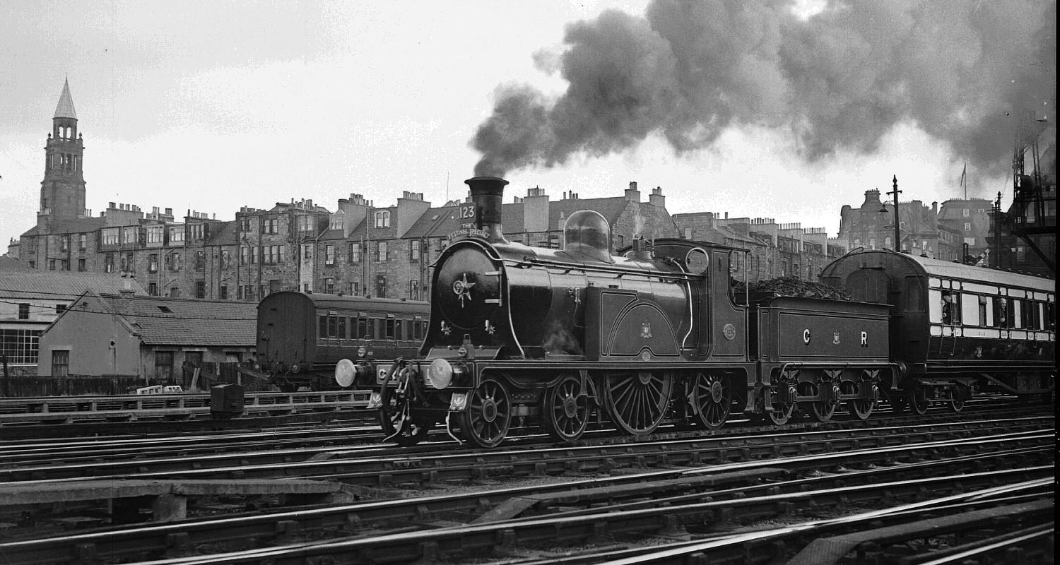 A black and white photo of a steam train travelling through the city