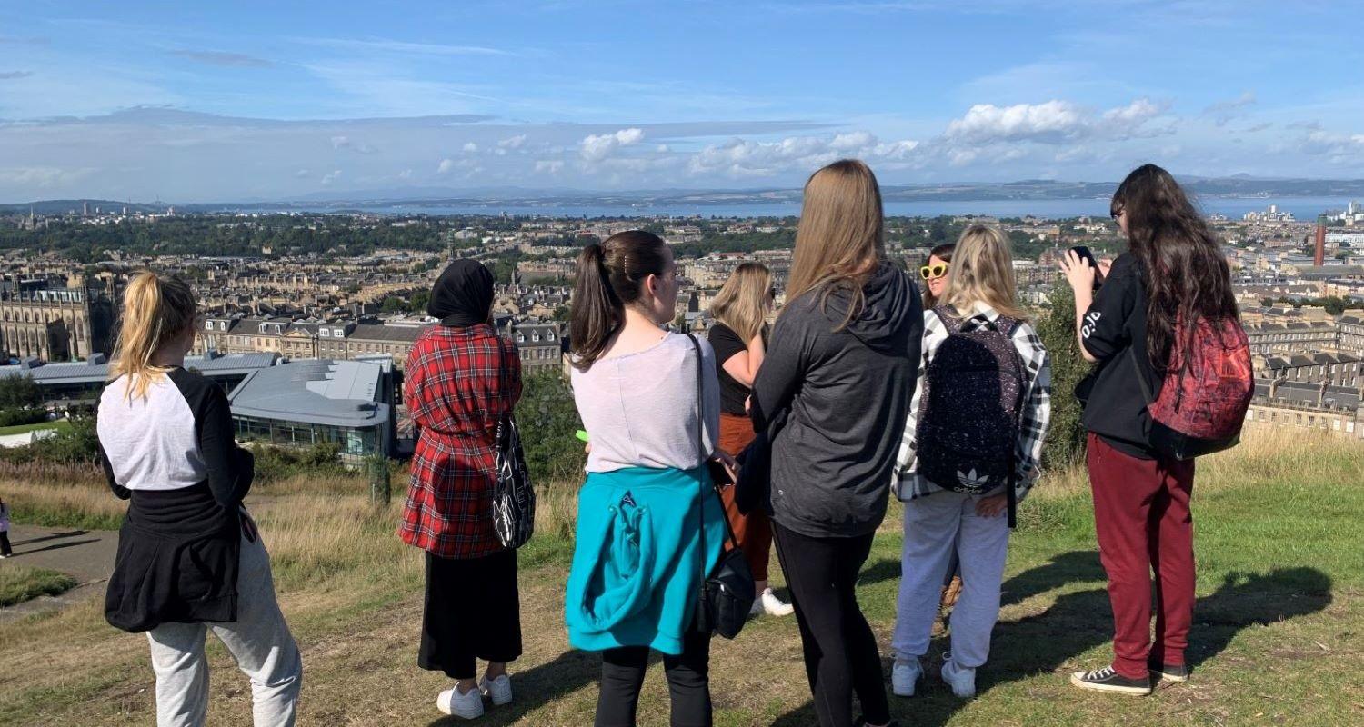 Group of  young people on Calton Hill looking over Edinburgh towards the Forth. 