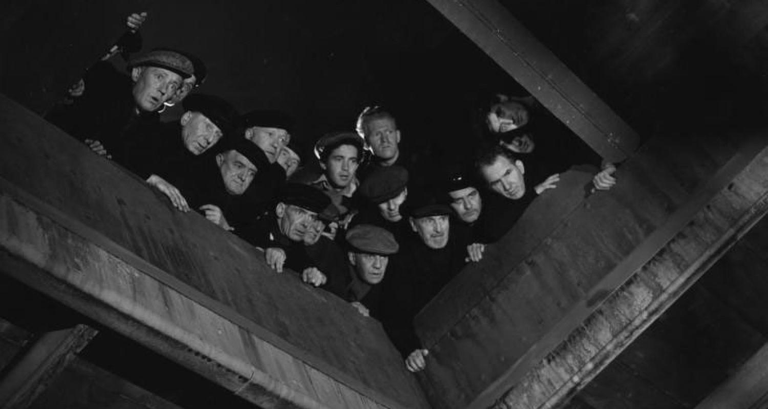 A black and white still of a group of men looking down the hatch on a boat - from the film version of Whisky Galore