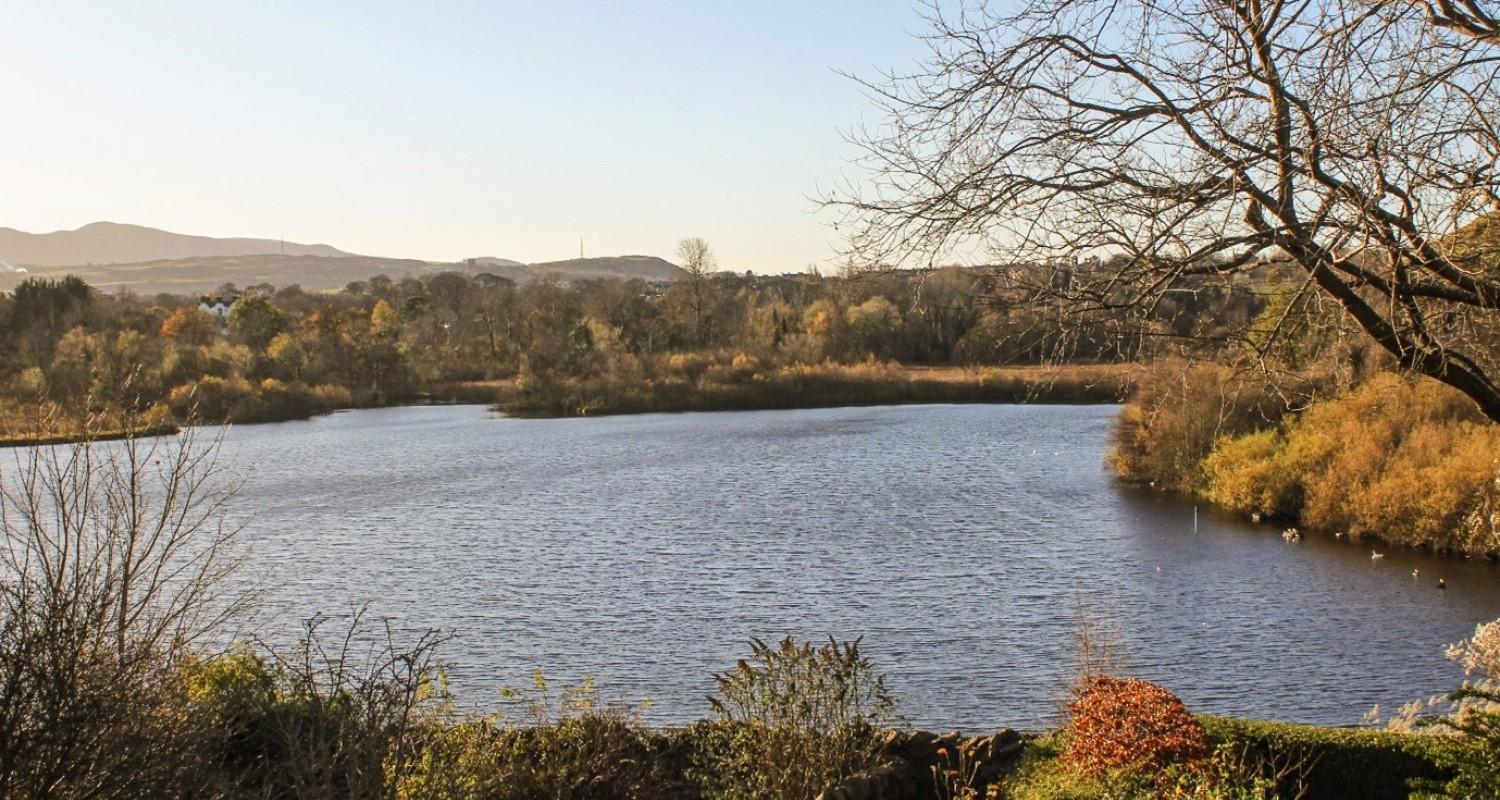 A landscape photo of a stretch of water surrounded by autumnal trees and hills