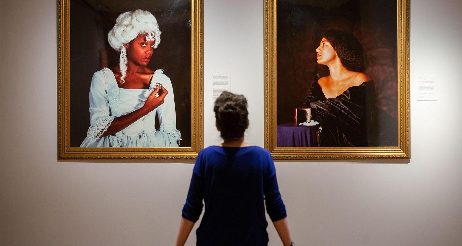 Curator sits admiring two paintings on display - both paintings are in gold frames