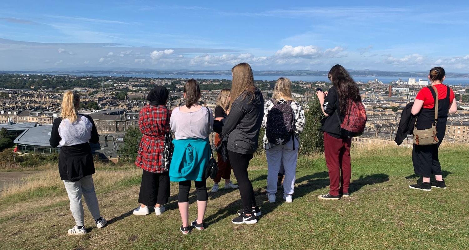A group of young people stand on a hill in Edinburgh and face Scotland's capital below