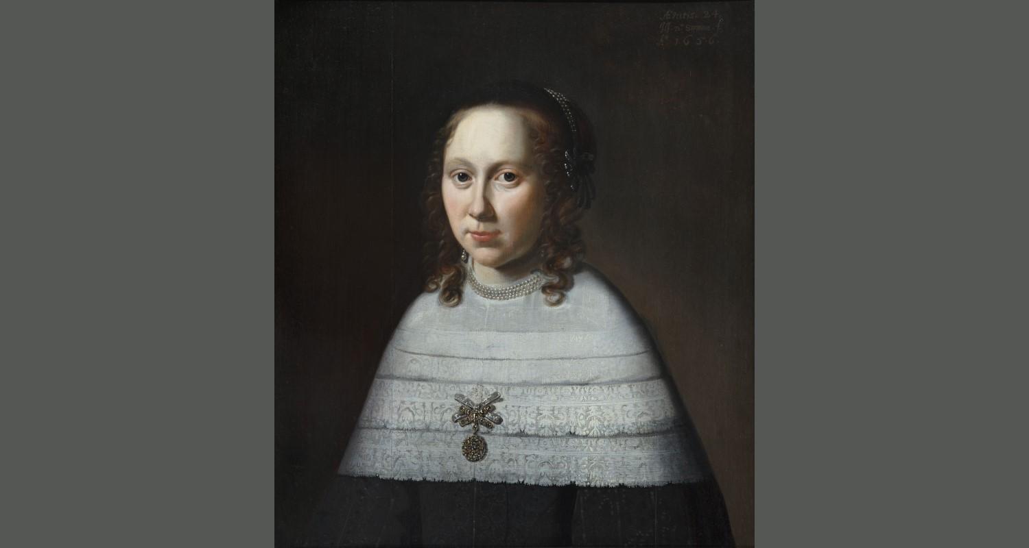 A portrait of a woman with shoulder length curly hair, wearing a white layered shawl round her shoulders, attached by a silver drop  brooch