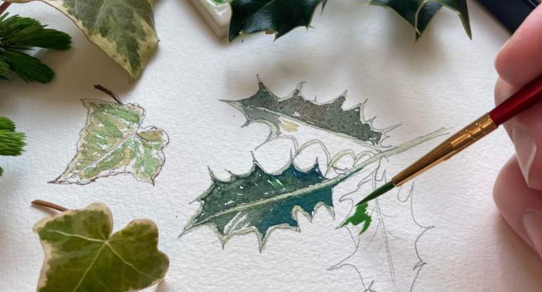 Photo of a person painting ivy and holly leaves on a  piece of white paper
