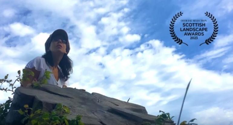 Anna Dako wearing sunglasses and a cap, sitting on a rock.