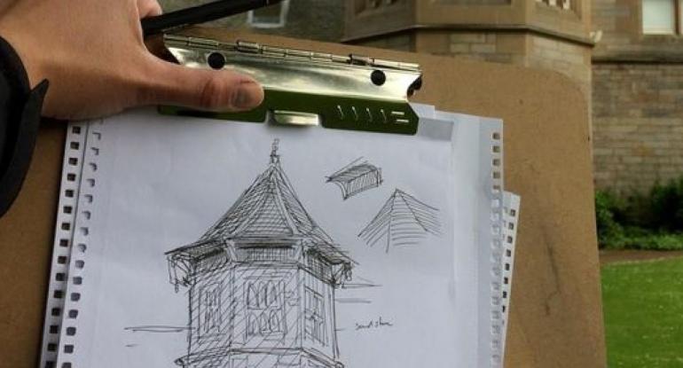 A hand holding a clipboard with a pencil sketch of the Castle