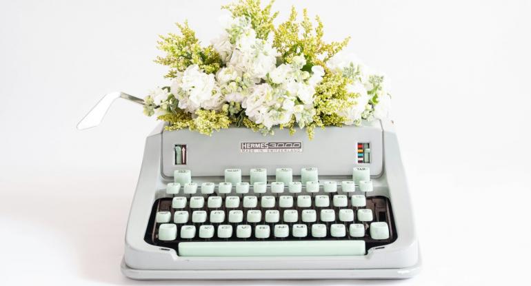 A manual typewriter against a white background with a flower on top