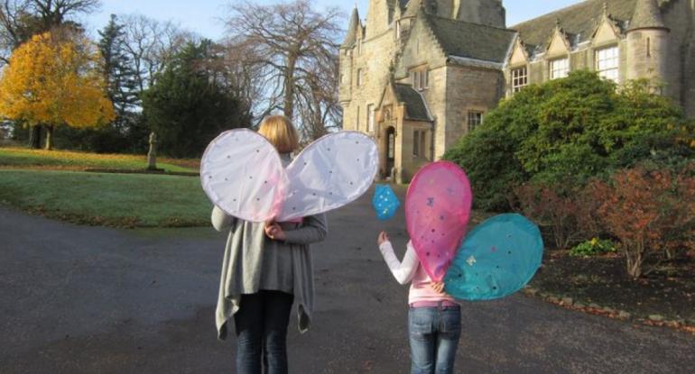 Rear view of an adult and child wearing fairy wings outside the castle