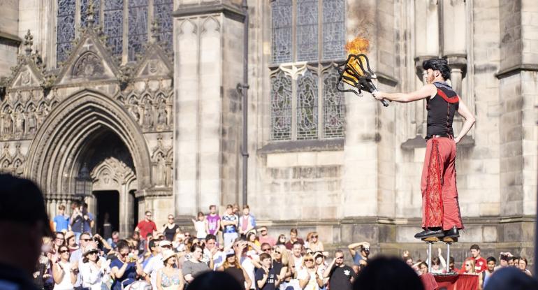 A fire eater holding flaming torches surrounded by crowds outside St Giles' cathedral