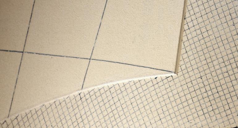 A piece of cream ceramic tile with line markings and a mesh of markings underneath