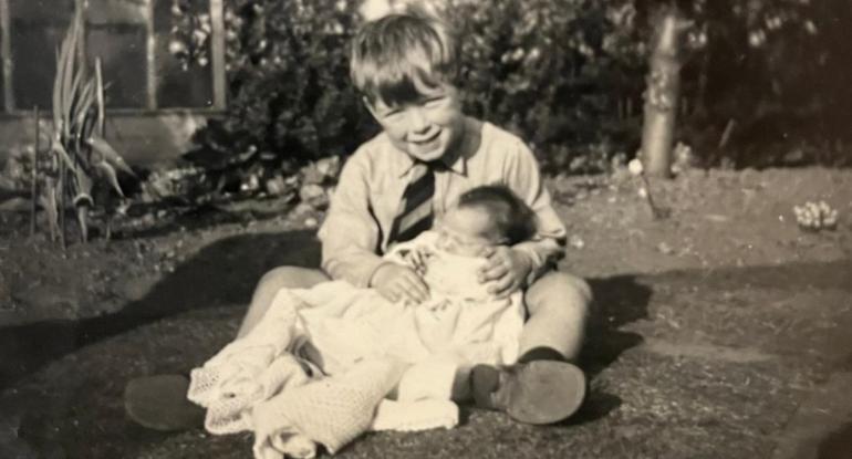 Gordon Roberts sitting in the back garden of his childhood home with his baby sister Frances wrapped in a shawl on his lap