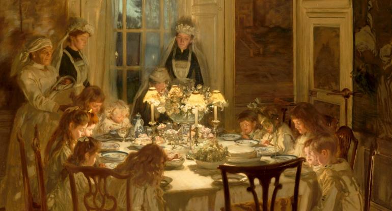 Edwardian children sitting round a dinner table with their maids