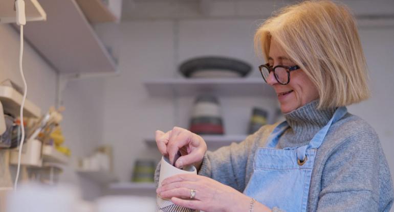 Lara Scobie, in blue dungarees and a grey jumper, working on a ceramic piece