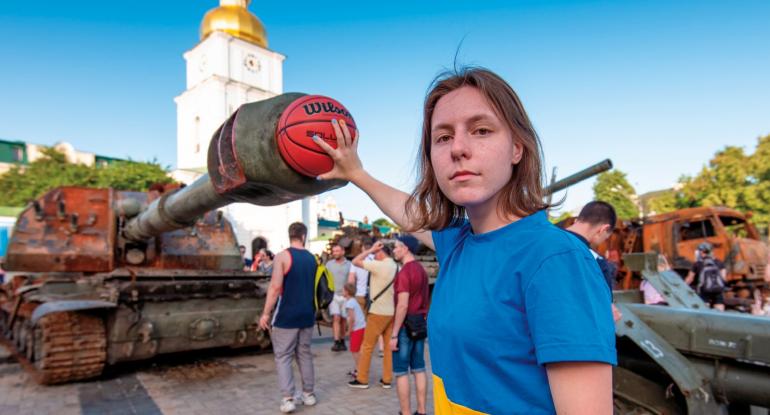 Young girl wearing a blue t-shirt, holds a basketball at the barrell of a tank