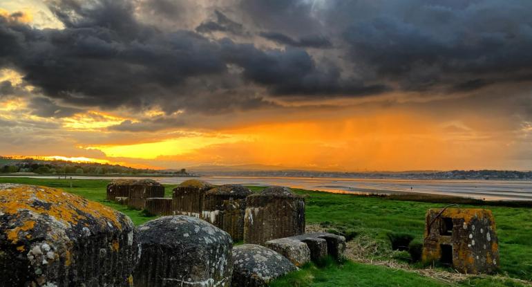 Sunset at Tentsmuir with a golden sky, dark clouds, and grass and stones in the foreground