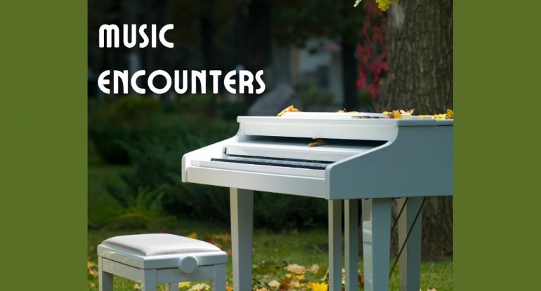 A white piano and piano stool standing on grass and surrounded by autumn leaves