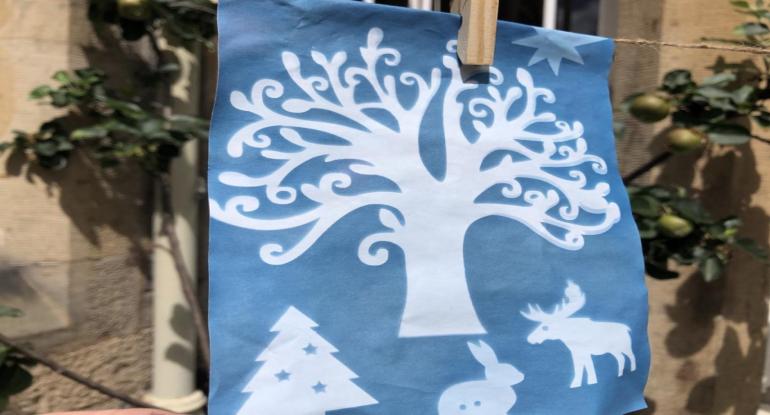A white tree, Xmas tree, stag and rabbit on a blue sheet of paper pegged onto a washing line