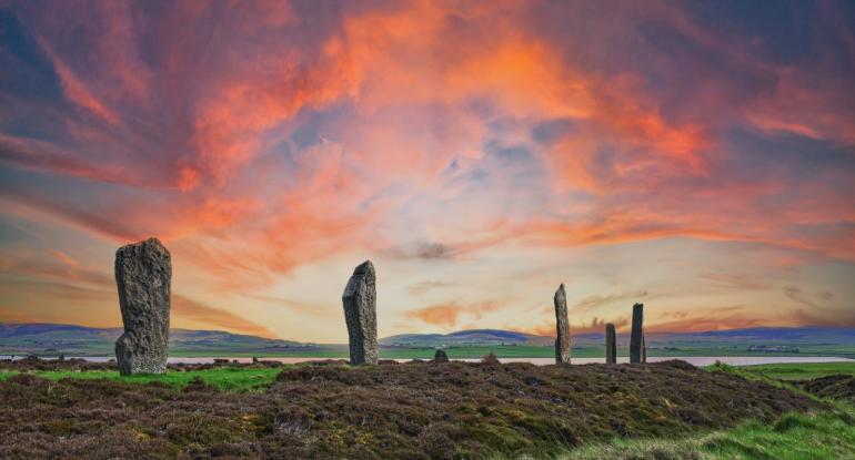 Standing stones on a grassy hillside against a red sunset