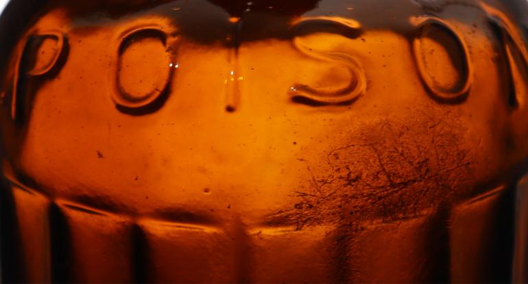 Close-up of the word "poison" embossed on a brown ridged glass bottle