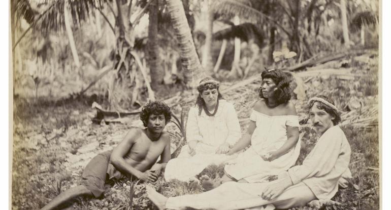 Robert Louis Stevensons in company with Nantoki and Natakauti, Butaritari. Group comprising of Nantoki, Fanny Stevenson holding hands with Natakauti, and Robert Louis Stevenson; the men are reclining, the women sitting, on the ground. 