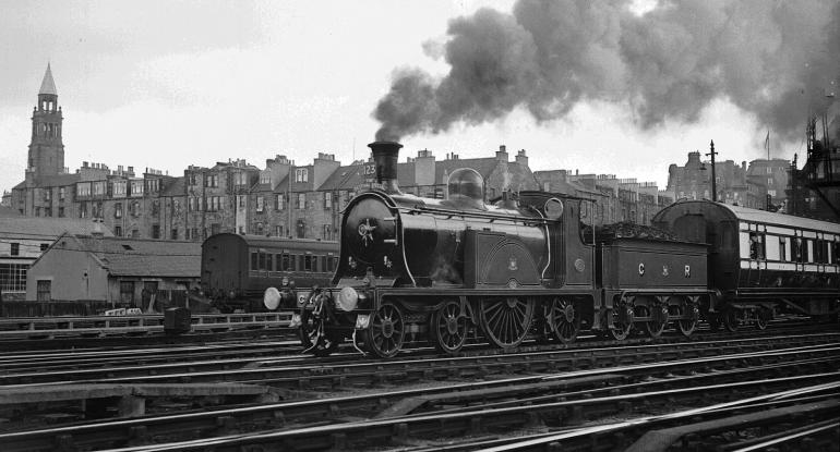 A black and white photo of a steam train travelling through the city