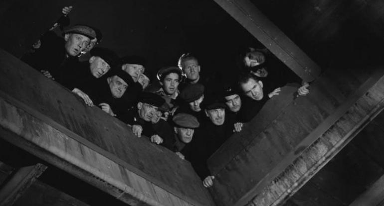 A black and white still of a group of men looking down the hatch on a boat - from the film version of Whisky Galore